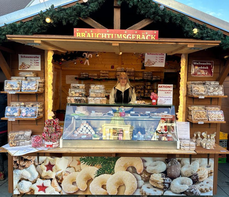 Weihnachtlich geschmückter Kekswerk-Stand mit Weihnachtsgebäck und Schaumrollen auf dem Christkindlmarkt
